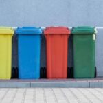 Recycling - four assorted-color trash bins beside gray wall