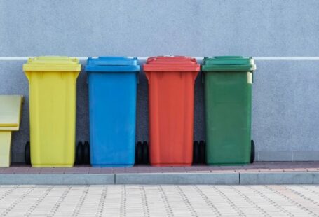 Recycling - four assorted-color trash bins beside gray wall